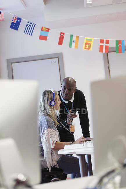 Community college instructor helping student with headphones at computer in computer lab classroom — Stock Photo