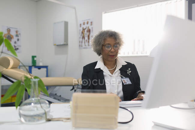 Médica sênior do sexo feminino que trabalha no computador no consultório — Fotografia de Stock