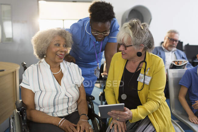 Female doctor with digital tablet talking to senior patient in wheelchair in clinic lobby — Stock Photo
