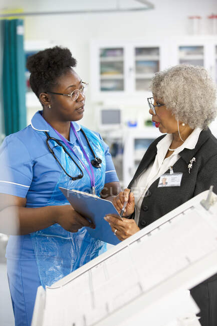 Doctora y enfermera con portapapeles hablando en el hospital - foto de stock