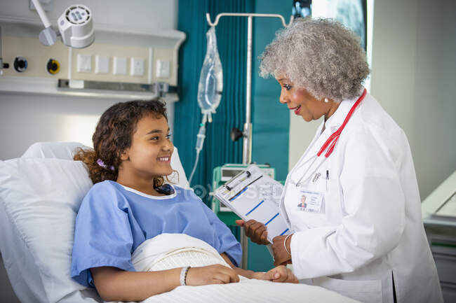 Female doctor talking with girl patient in hospital room — Stock Photo