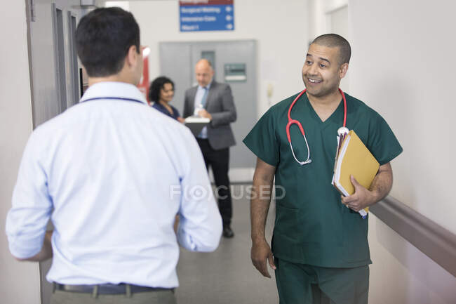 Lächelnder Chirurg grüßt vorbeifahrenden Arzt auf Krankenhausflur — Stockfoto