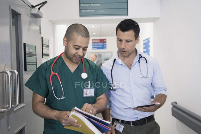 Чоловік, лікар і хірург обговорюють медичну карту, а тоді обходять лікарняний коридор. — стокове фото