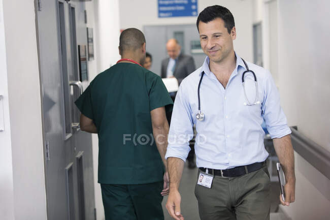 Médico varón con tableta digital caminando por el pasillo del hospital - foto de stock