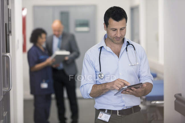 Чоловік лікар використовує цифровий планшет в лікарняному коридорі — стокове фото
