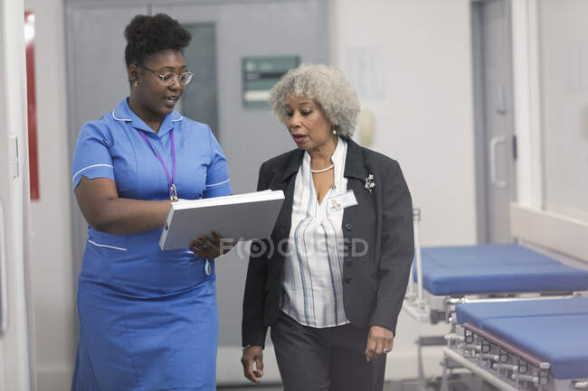 Ärztin und Krankenschwester diskutieren medizinische Diagramme und drehen ihre Runden im Krankenhausflur — Stockfoto