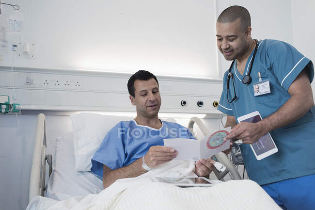 Paciente masculino mostrando tarjeta de felicitación a la enfermera en la habitación del hospital - foto de stock