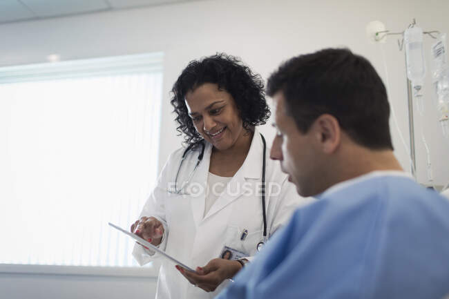 Врач с цифровыми таблетками делает обходы, разговаривает с пациентом в больничной палате — стоковое фото