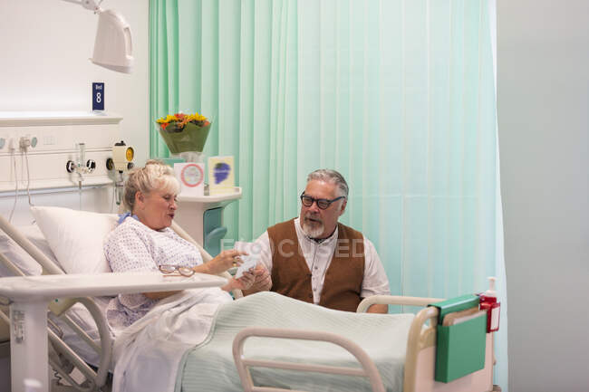Hombre mayor visitando esposa descansando en la habitación del hospital - foto de stock