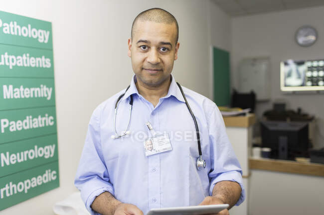 Portrait confident male doctor with digital tablet in hospital corridor — Stock Photo