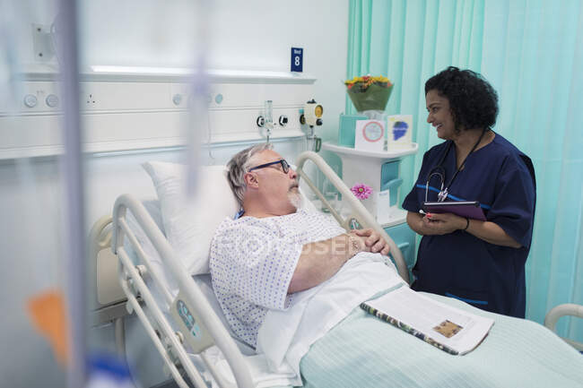 Doctor con tableta digital haciendo rondas, hablando con pareja mayor en la habitación del hospital - foto de stock