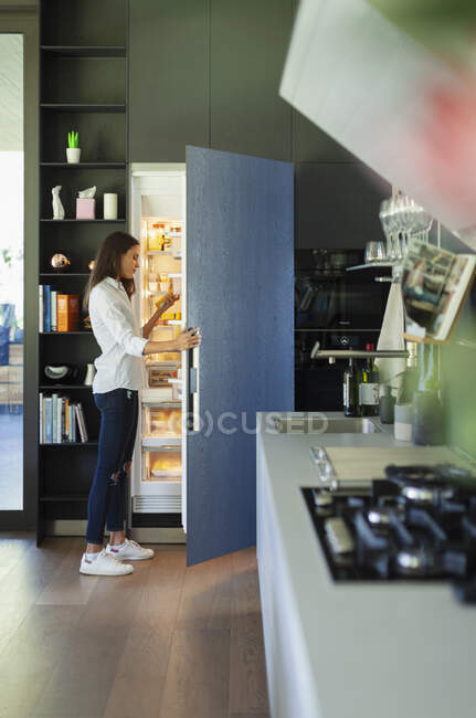 Mulher de pé na geladeira aberta na cozinha — Fotografia de Stock