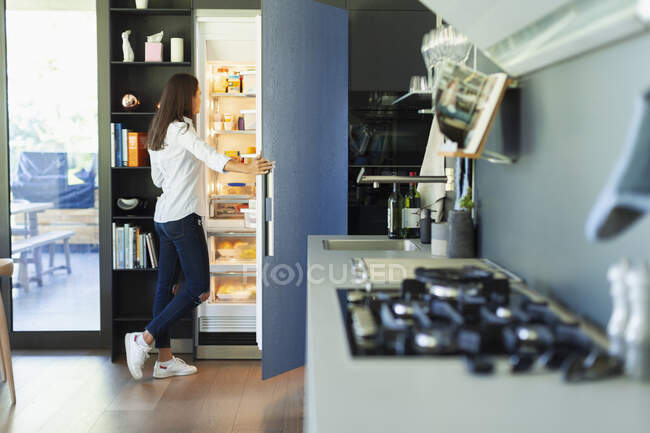 Woman standing at open refrigerator in kitchen — Stock Photo