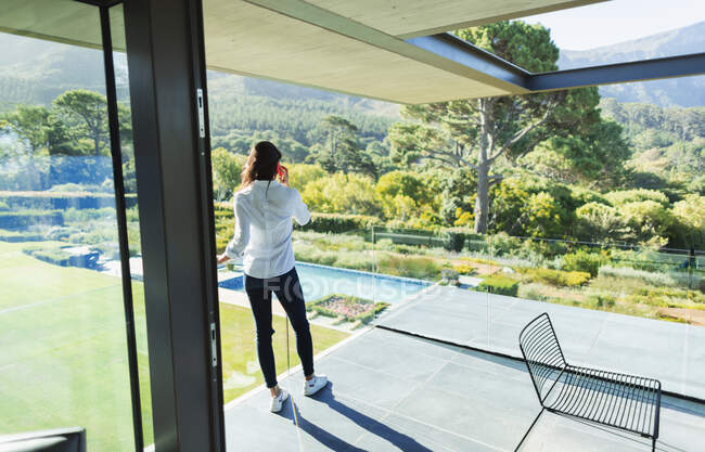 Femme parlant sur téléphone intelligent sur balcon de luxe ensoleillé avec vue — Photo de stock
