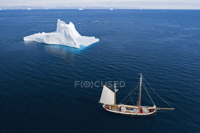 Navio de vela passado iceberg majestoso no azul ensolarado Oceano Atlântico Groenlândia — Fotografia de Stock