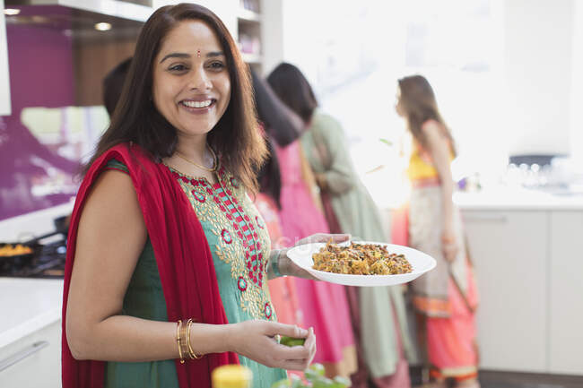Portrait happy Indian woman in sari eating in kitchen — Stock Photo