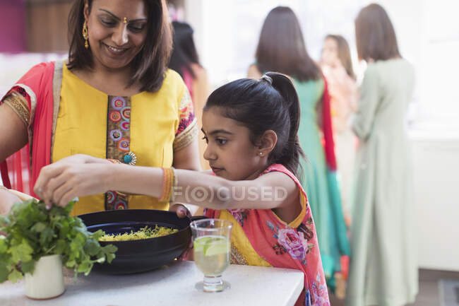 Madre e hija india en saris cocinando con hierba fresca en la cocina - foto de stock