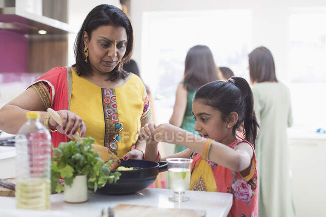 Madre e hija india en saris cocinando comida en la cocina - foto de stock