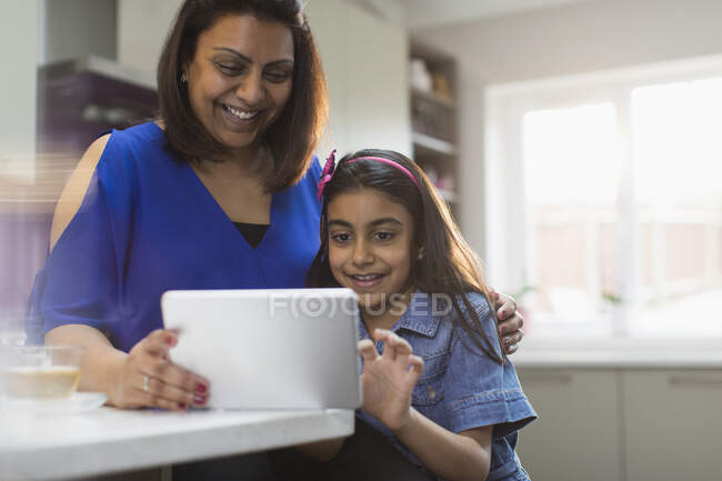 Счастливые мама и дочь с помощью цифрового планшета на кухне — стоковое фото