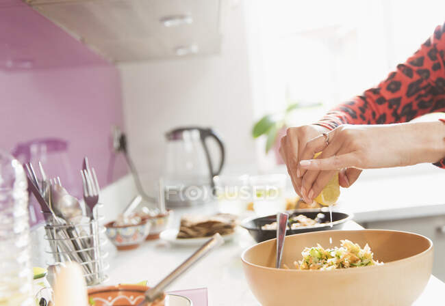 Woman squeezing lemon over bowl of food in kitchen — Stock Photo