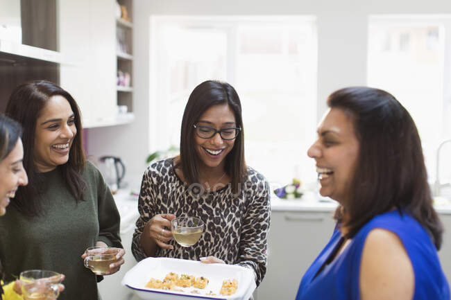 Happy Indian women with tea and food in kitchen — Stock Photo