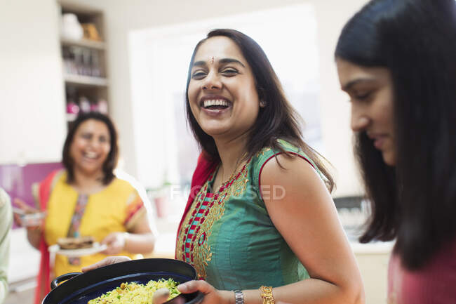 Mujer india feliz en sari preparando comida con la familia en la cocina - foto de stock