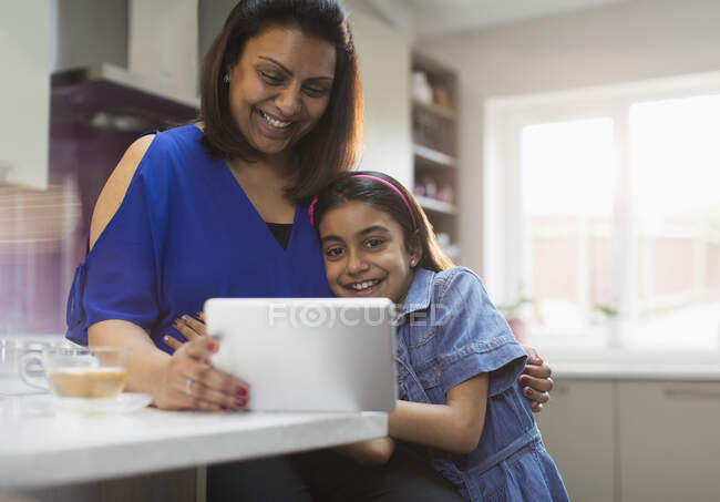 Улыбающиеся мать и дочь с помощью цифрового планшета на кухне — стоковое фото
