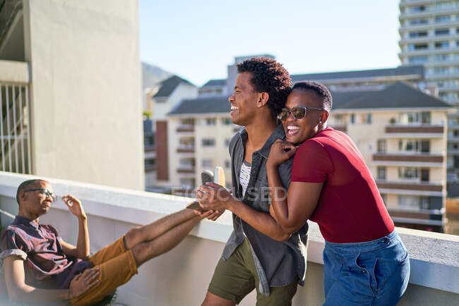 Felice giovane coppia ridendo e abbracciando sul balcone urbano soleggiato — Foto stock