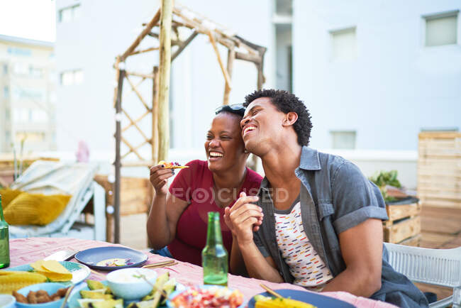 Feliz jovem casal rindo e comendo na mesa do pátio — Fotografia de Stock