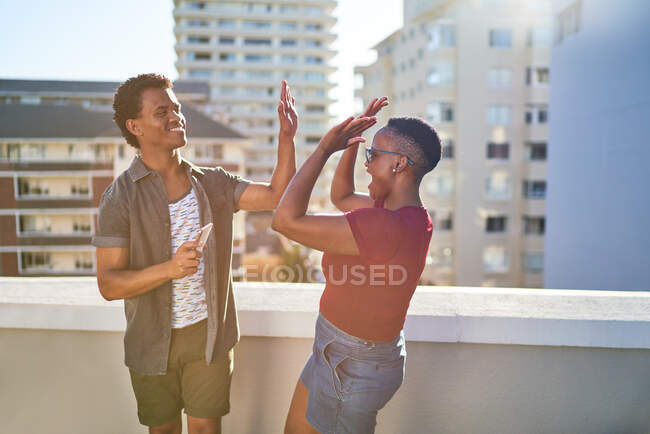 Happy young couple high fiving on sunny urban rooftop balcony — Stock Photo