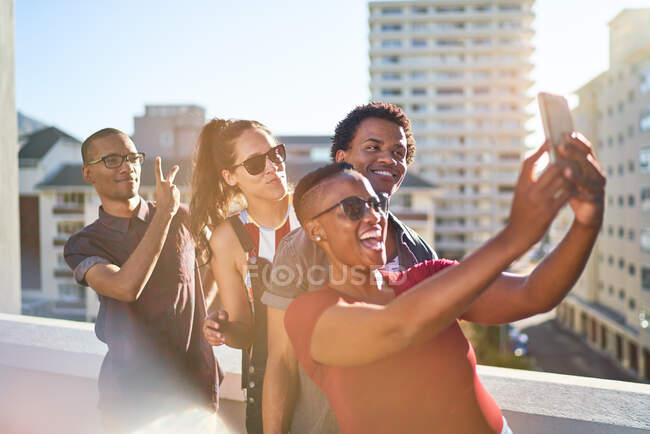 Jóvenes amigos usando el teléfono inteligente en el balcón soleado de la azotea urbana - foto de stock
