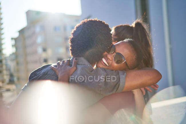 Feliz joven pareja abrazándose en el soleado balcón urbano - foto de stock