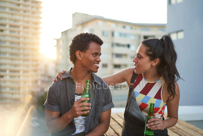Feliz joven pareja bebiendo cerveza en el soleado balcón de la azotea urbana - foto de stock