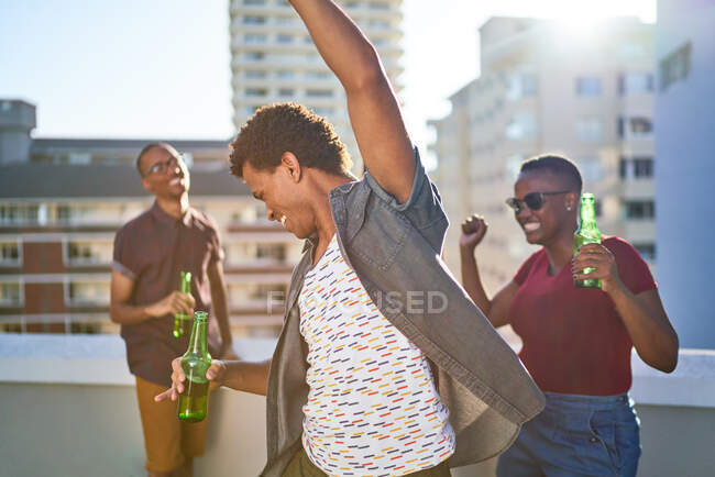 Unbekümmerte junge Freunde tanzen und trinken Bier auf sonnigem Dach — Stockfoto