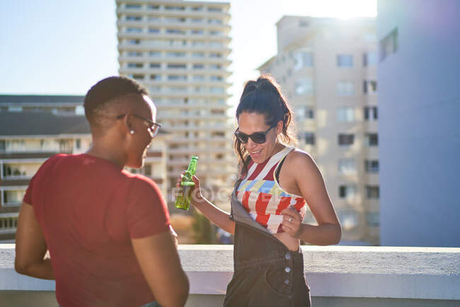 Carefree young woman dancing and drinking beer on sunny urban rooftop — Stock Photo