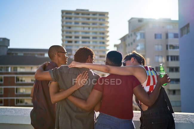 Young friends hugging on sunny urban rooftop balcony — Stock Photo