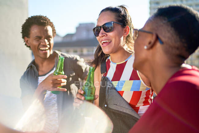 Happy young friends drinking beer on sunny balcony — Stock Photo