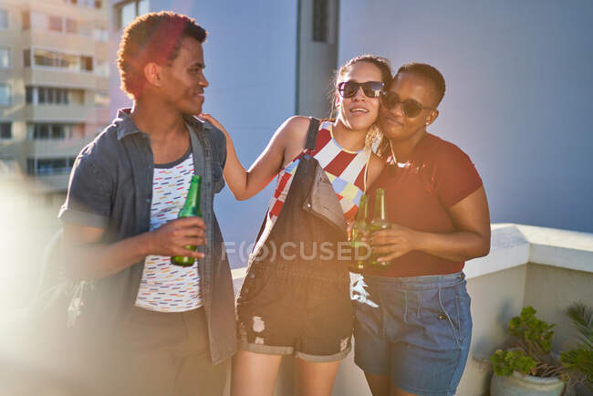 Felices jóvenes amigos bebiendo cerveza en el soleado balcón urbano - foto de stock