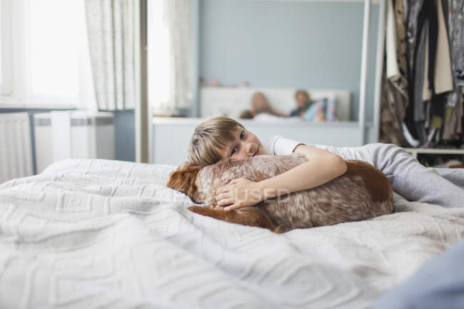 Портрет милый мальчик обнимает собаку на кровати — стоковое фото