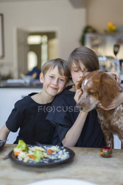 Portrait brothers with dog eating at dining table — Stock Photo
