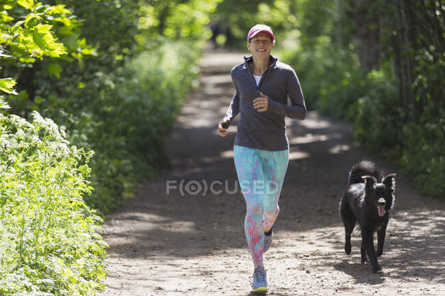 Mulher correndo com cão em trilha ensolarada — Fotografia de Stock