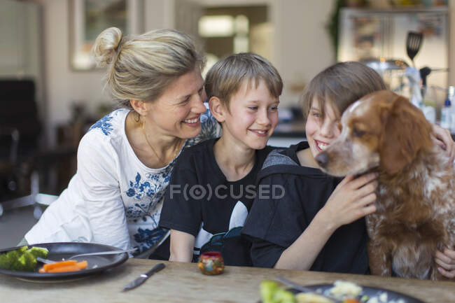 Happy mother and sons with dog at dinner table — Stock Photo