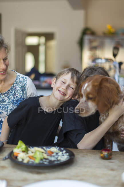 Família feliz com cão almoçando na mesa de jantar — Fotografia de Stock