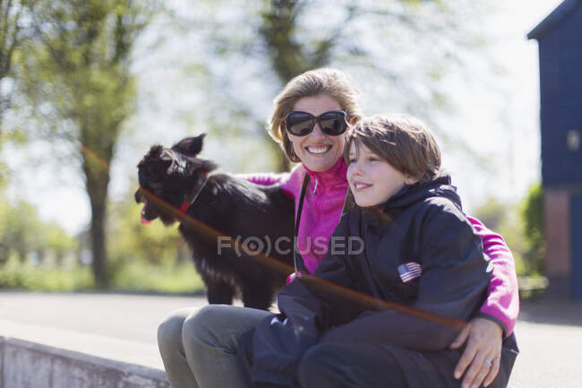 Retrato feliz madre e hijo con perro en la cornisa soleada - foto de stock