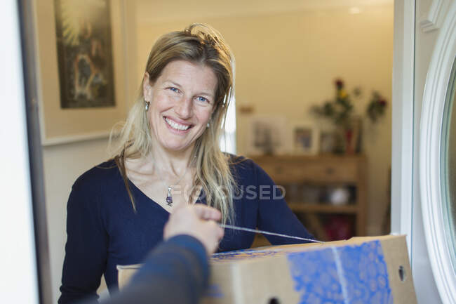 Retrato sonriente mujer recibiendo el parto en la puerta principal - foto de stock