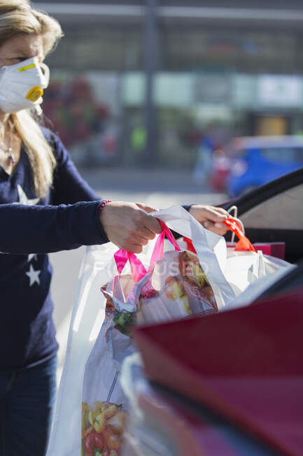 Женщина в маске для лица выгружает продукты из машины — стоковое фото