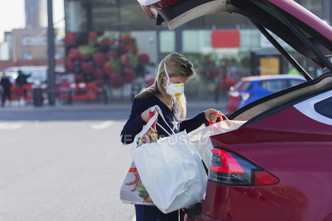 Frau mit Gesichtsmaske lädt Lebensmittel auf Parkplatz in Auto — Stockfoto