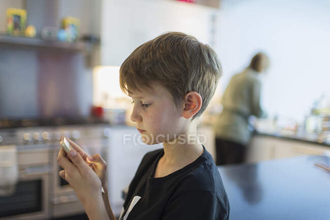 Niño usando el teléfono inteligente en la cocina - foto de stock