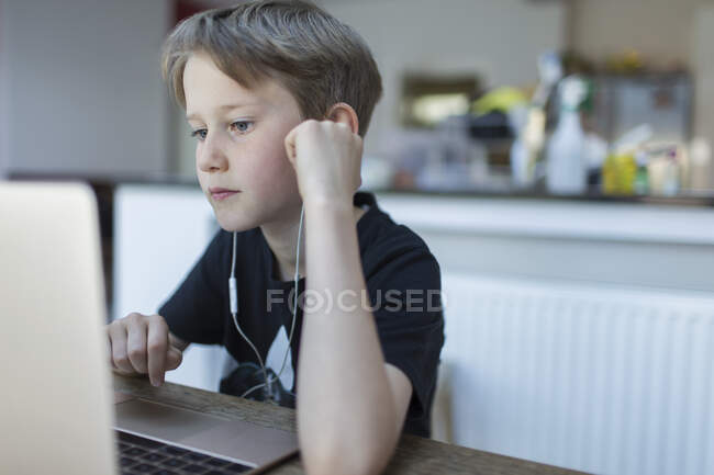 Menino focado com fones de ouvido em casa no laptop — Fotografia de Stock