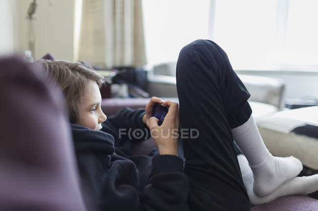 Menino jogando jogo de vídeo com telefone inteligente no sofá — Fotografia de Stock